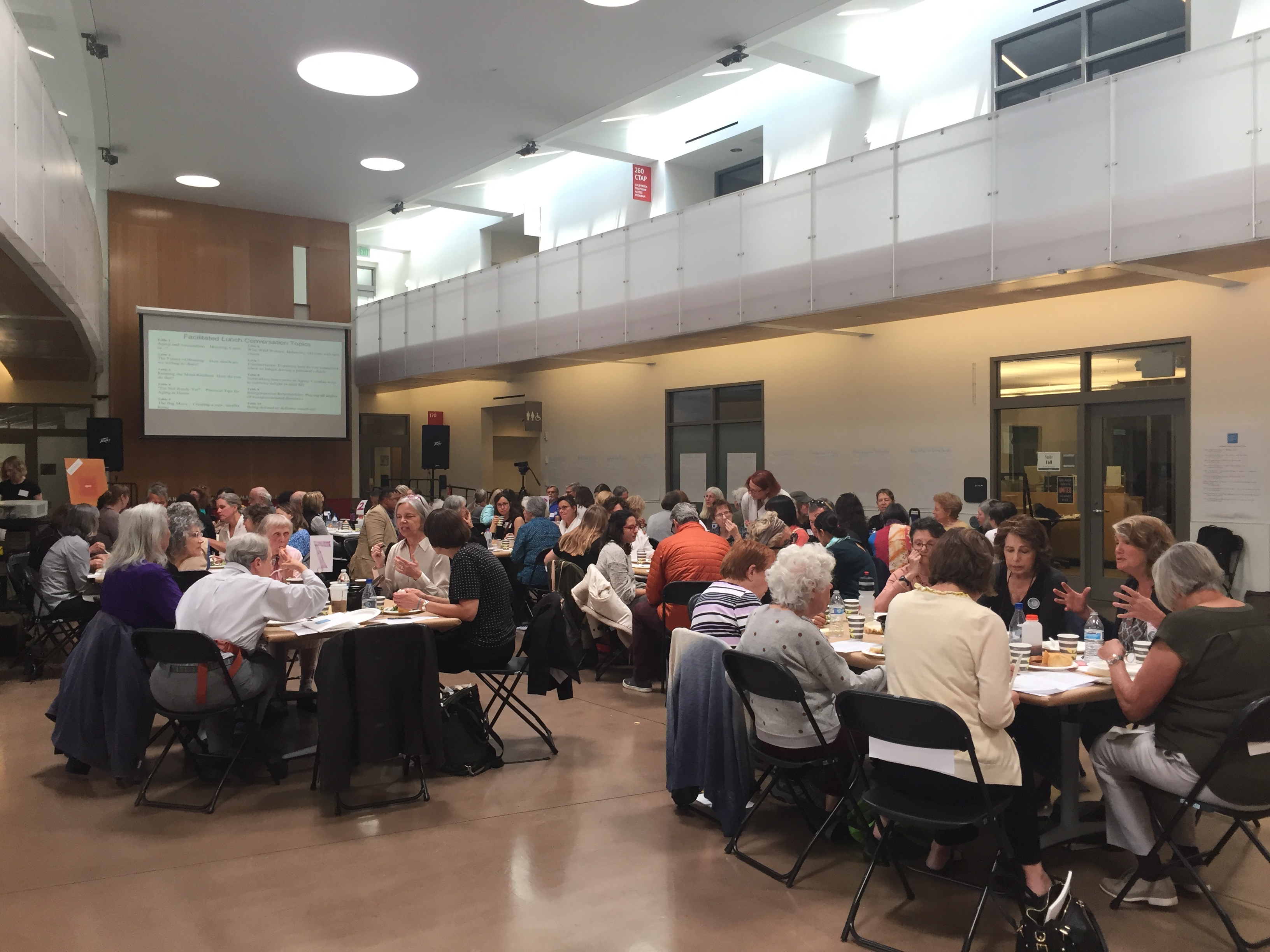 People gathered around small tables in a large room, talking amongst themselves.